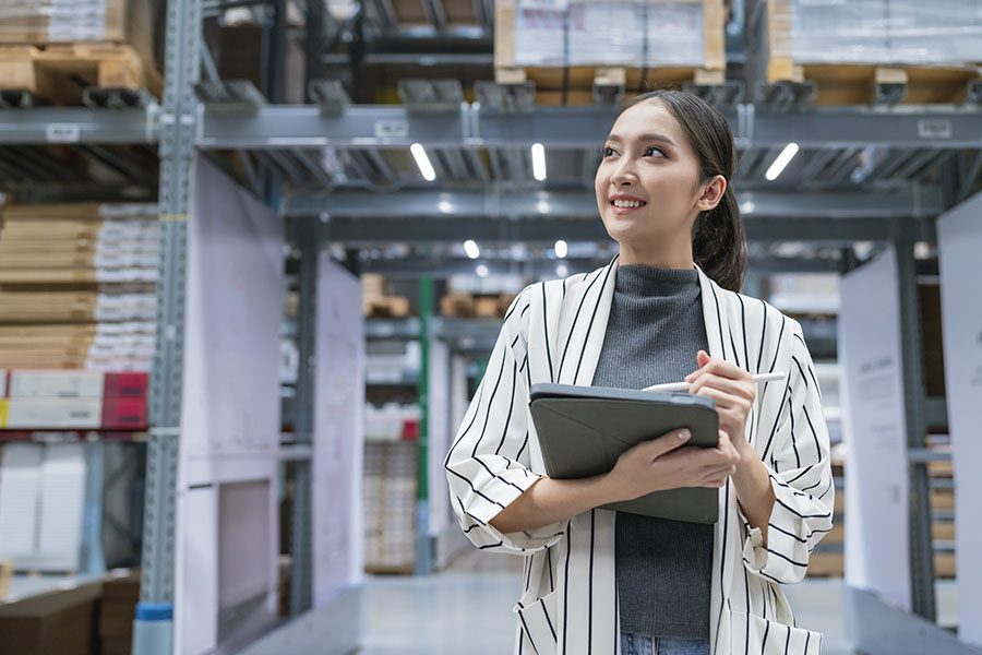 Business Insurance - Portrait of a Smiling Young Business Woman Standing in a Warehouse While Holding a Tablet in Her Hands