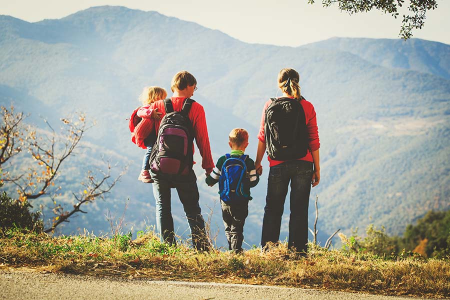 Personal Insurance - Back View of a Family with Two Kids Wearing Backpacks Looking Ahead at the Mountains as They Start Their Hike on a Sunny Day